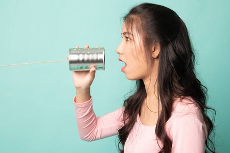 Young Asian woman shout with tin can phone on cyan backgroundの写真素材