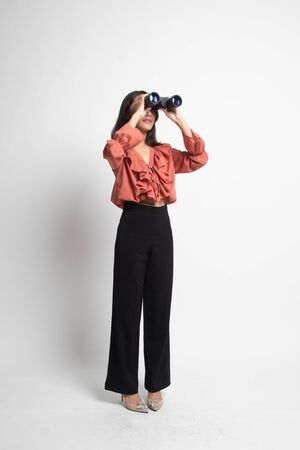 Full body of young Asian woman with binoculars on white backgroundの写真素材