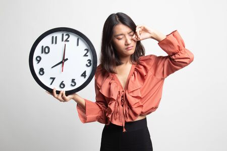 Sleepy young Asian woman with a clock in the morning on white backgroundの写真素材