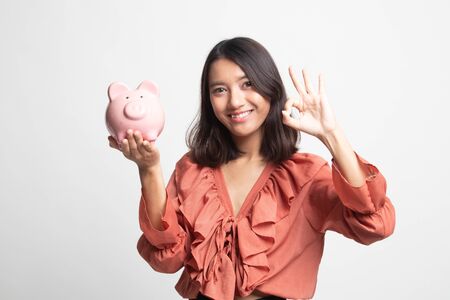 Asian woman show OK  with pig coin bank on white backgroundの写真素材