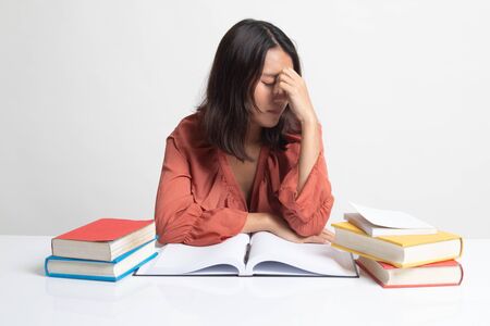 Exhausted Asian woman got headache read a book with books on table on white backgroundの写真素材