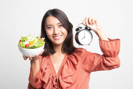 Young Asian woman with clock and salad on white backgroundの写真素材