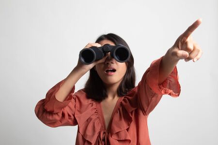 Young Asian woman  point and look with binoculars on white backgroundの写真素材