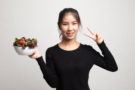 Healthy Asian woman show victory sign with salad on white backgroundの写真素材