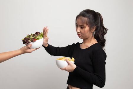 Young Asian woman with potato chips say no to salad on white backgroundの写真素材
