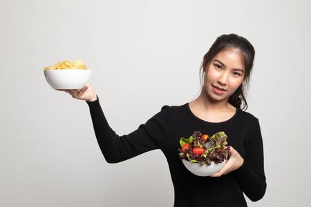 Young Asian woman with potato chips and salad on white backgroundの写真素材
