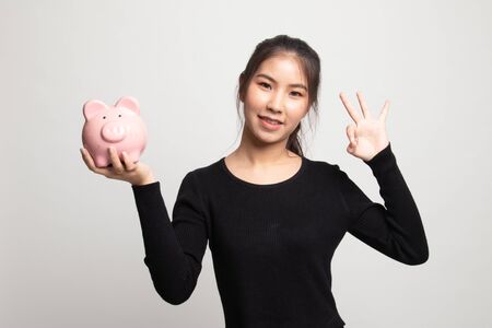 Asian woman show OK  with pig coin bank on white backgroundの写真素材