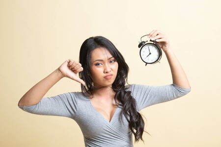Young Asian woman thumbs down with a clock   on beige backgroundの写真素材