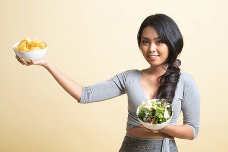 Young Asian woman with potato chips and salad   on beige backgroundの写真素材