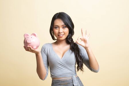 Asian woman show OK  with pig coin bank   on beige backgroundの写真素材
