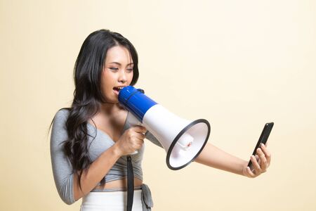 Angry  young Asian woman shout with megaphone to mobile phone   on beige backgroundの写真素材