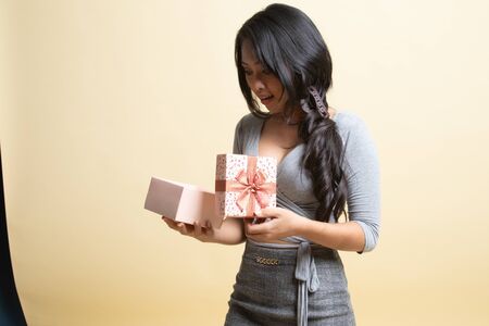 Young Asian woman open a golden gift box   on beige backgroundの写真素材