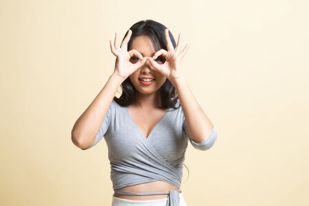 Asian woman do funny  double OK sign as glasses   on beige backgroundの写真素材