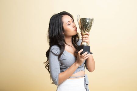 Successful young asian woman holding kissing a trophy   on beige backgroundの写真素材