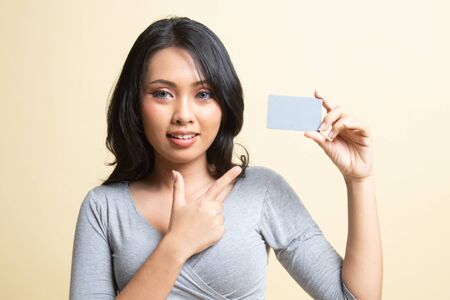 Young Asian woman point to a blank card   on beige backgroundの写真素材