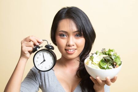 Young Asian woman with clock and salad   on beige backgroundの写真素材