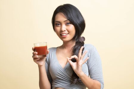 Young Asian woman show OK with tomato juice   on beige backgroundの写真素材