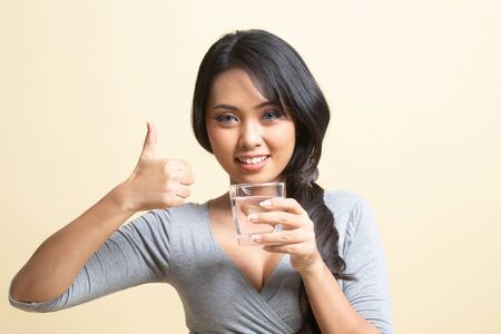 Young Asian woman thumbs up with a glass of drinking water   on beige backgroundの写真素材