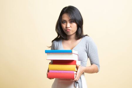 Unhappy young Asian woman studying  with may books   on beige backgroundの写真素材