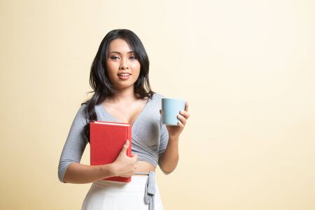 Young Asian woman with a book and cup of coffee   on beige backgroundの写真素材