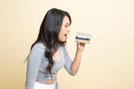 Young Asian woman shout with tin can phone   on beige backgroundの写真素材