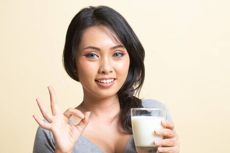 Healthy Asian woman drinking a glass of milk show OK sign   on beige backgroundの写真素材