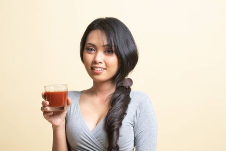 Young Asian woman drink tomato juice   on beige backgroundの写真素材