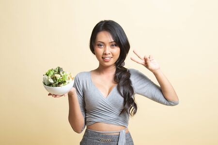Healthy Asian woman show victory sign with salad   on beige backgroundの写真素材