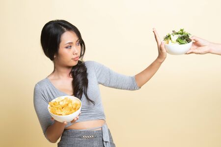 Young Asian woman with potato chips say no to salad   on beige backgroundの写真素材