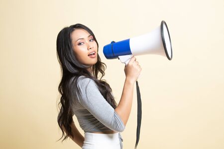 Beautiful young Asian woman announce with megaphone   on beige backgroundの写真素材