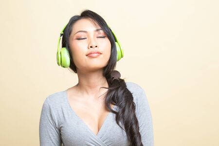 Pretty asian girl listening music with her headphones   on beige backgroundの写真素材