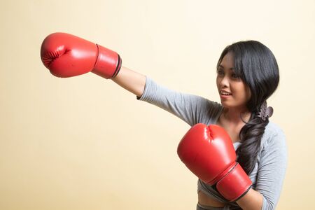 Young Asian woman with red boxing gloves   on beige backgroundの写真素材