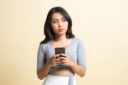 Young Asian woman with mobile phone   on beige backgroundの写真素材