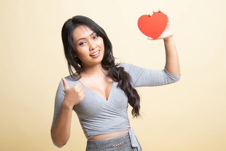 Asian woman thumbs up with red heart   on beige backgroundの写真素材