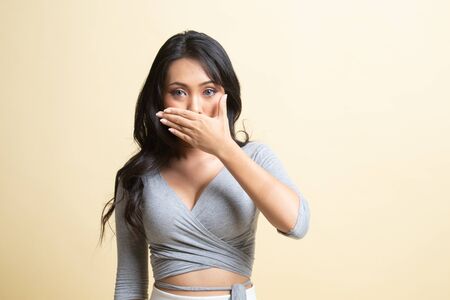 Young Asian woman close her mouth with hand   on beige backgroundの写真素材