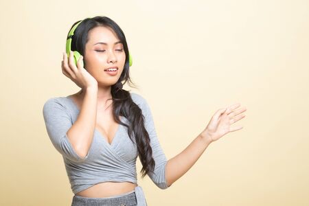 Pretty asian girl listening music with her headphones   on beige backgroundの写真素材