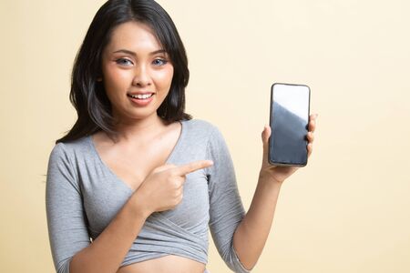 Young Asian woman point to mobile phone   on beige backgroundの写真素材