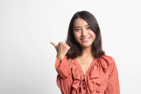 Young Asian woman smile and point to copy space with her thumb on white backgroundの写真素材