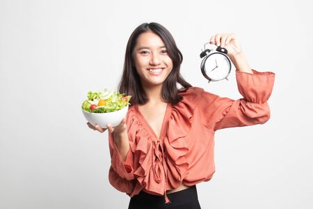 Young Asian woman with clock and salad on white backgroundの写真素材