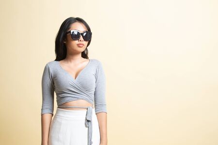 Portrait of a beautiful young asian girl in sunglasses   on beige backgroundの写真素材