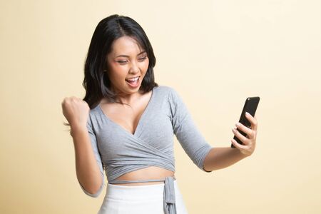 Successful young Asian woman with mobile phone   on beige backgroundの写真素材