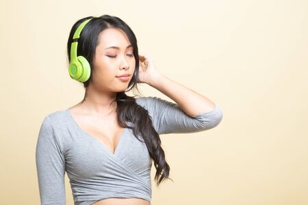 Pretty asian girl listening music with her headphones   on beige backgroundの写真素材