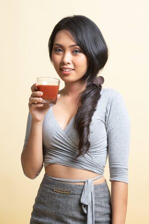 Young Asian woman drink tomato juice   on beige backgroundの写真素材