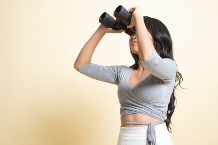 Young Asian woman with binoculars   on beige backgroundの写真素材