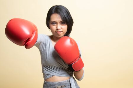 Young Asian woman with red boxing gloves   on beige backgroundの写真素材