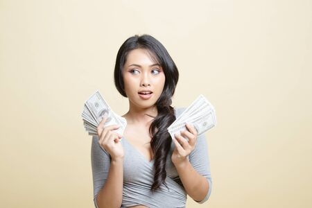Portrait of  young asian woman  showing bunch of money banknotes   on beige backgroundの写真素材