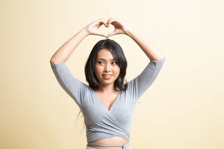 Young Asian woman gesturing heart hand sign   on beige backgroundの写真素材