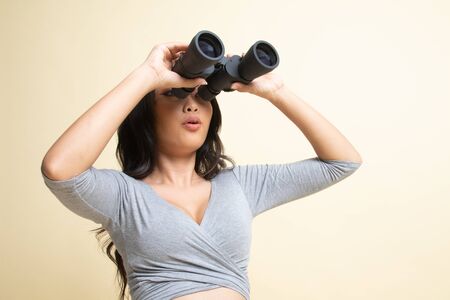 Young Asian woman with binoculars   on beige backgroundの写真素材