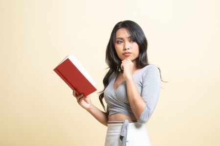 Young Asian woman with a book is thinking   on beige backgroundの写真素材