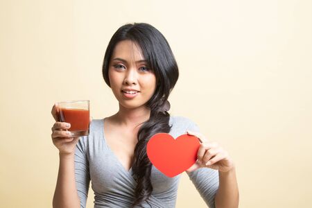 Young Asian woman with tomato juice and red heart   on beige backgroundの写真素材